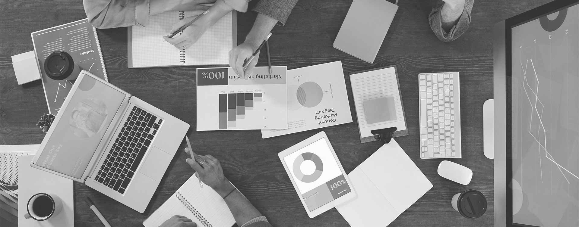 Value-innovation-group-sitting-at-work-desk-with-laptop-and-computer